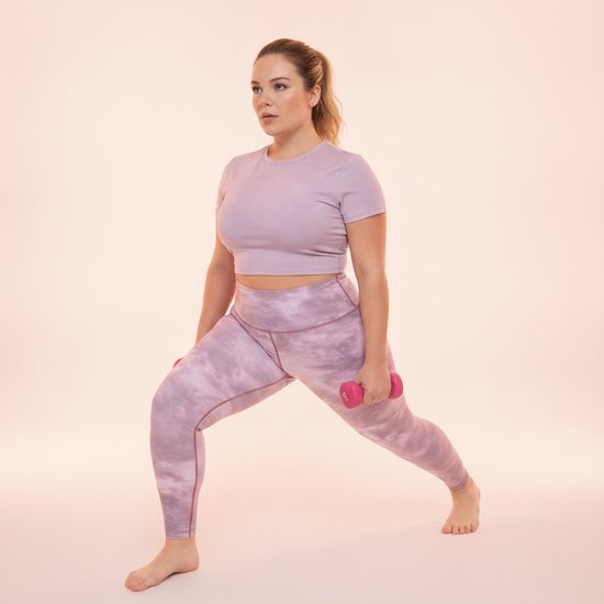 Vrouw in roze tie-dye legging en lila top, die een lunge-oefening doet met roze dumbbells.