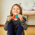 Een lachend meisje houdt een regenboogkleurig Plus-Plus figuurtje vast.