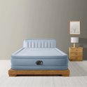 Blauw Intex luchtbed met ingebouwd hoofdbord, geplaatst op een houten frame in een slaapkamer.