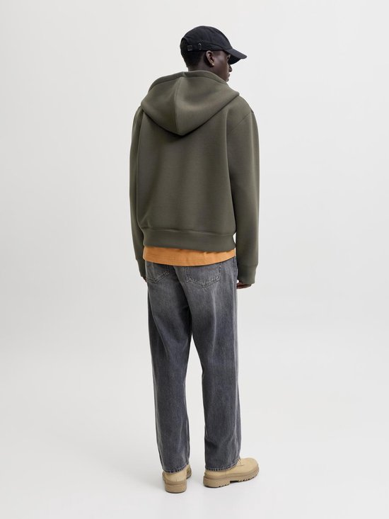 Model draagt donkergroene hoodie met ritssluiting, oranje T-shirt en spijkerbroek, zicht van achteren.