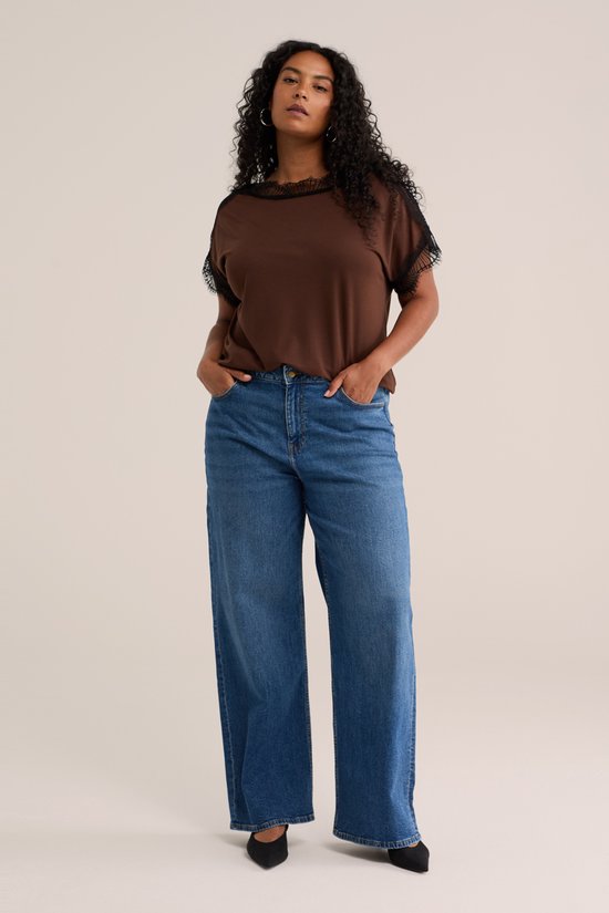 Model met bruin shirt met kanten details en wijde spijkerbroek met strik.
