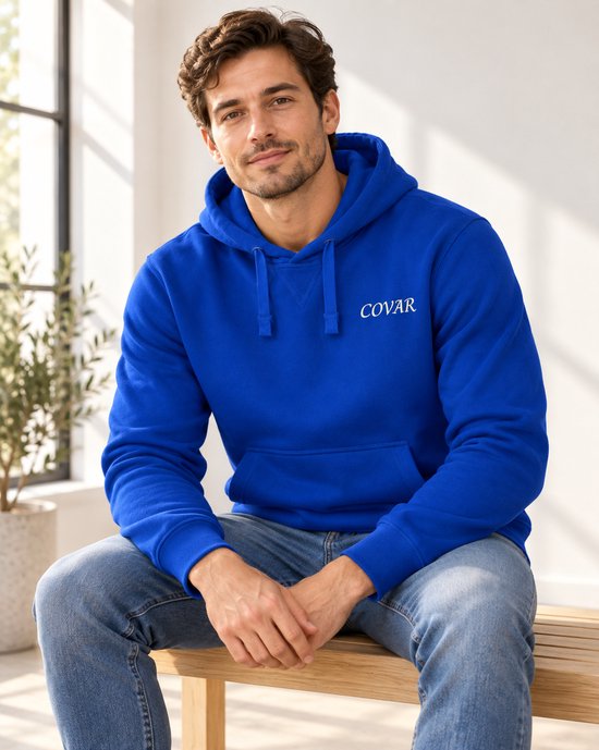 Model in koningsblauwe hoodie met capuchon en COVAR logo, zittend.