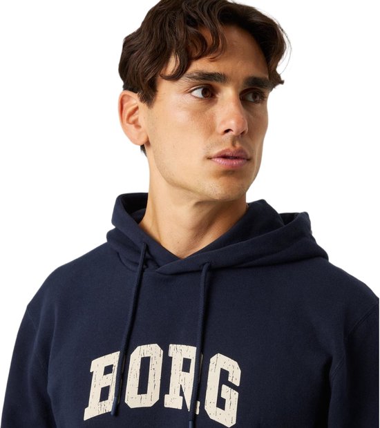 Close-up van een donkerblauwe hoodie met crèmekleurige 'BORG' tekst, gedragen door een man.