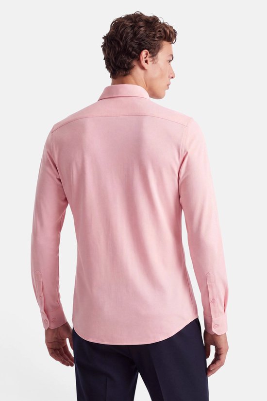 Achteraanzicht van een model in een roze overhemd met piqué textuur en donkere broek.