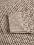 Close-up van de ribgebreide mouwboord van de beige polo.