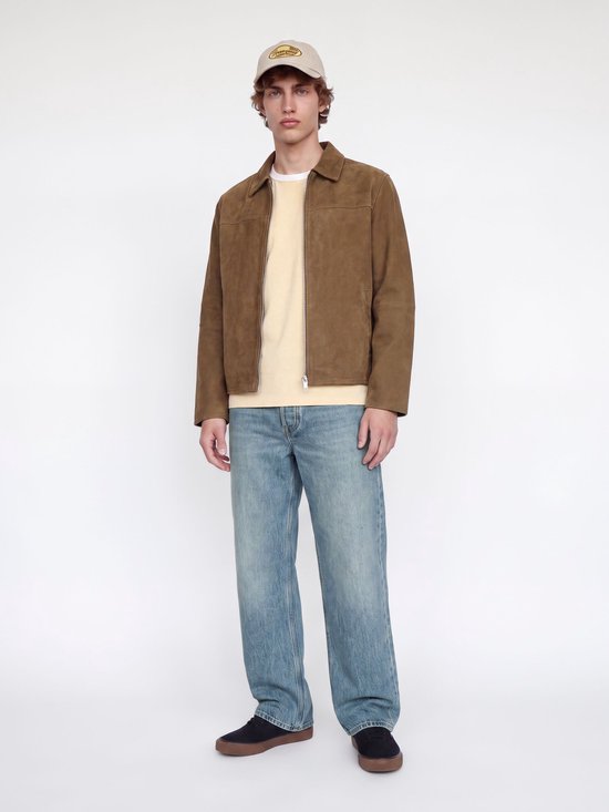 Model draagt een bruin suède jack, beige t-shirt, blauwe jeans en pet.