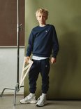 Jongen in een donkerblauwe sweater met logo en trainingsbroek, met een driehoek op schoolbord.