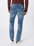 Lichtblauwe jeans met een verweerd effect, gedragen door een man met een bordeaux overhemd en witte sneakers.