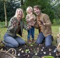Familie met modderige handen lacht in de tuin, omringd door plantuien.