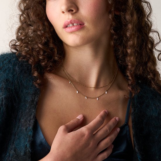 Model draagt een gouden dubbel collier met zilverkleurige druppels.
