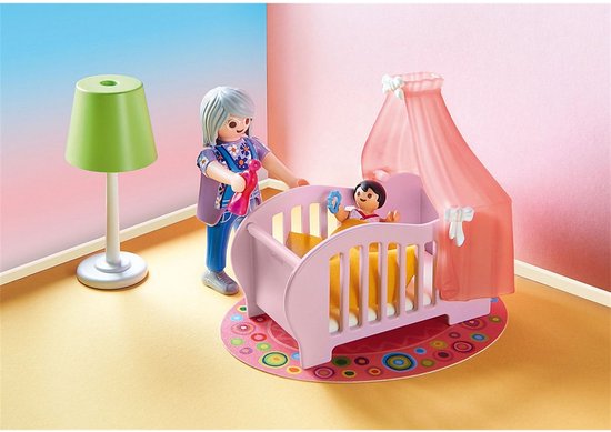 Een Playmobil oma staat bij een roze babywieg met hemel en een groene lamp, op een rond vloerkleed.
