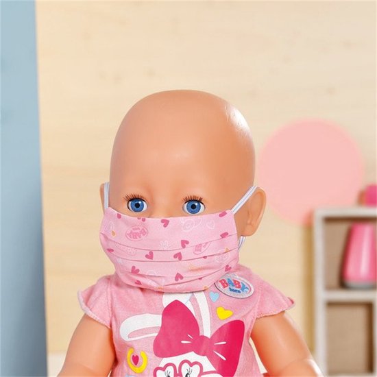 Close-up van een baby Born pop met een roze masker met hartjespatroon en een dokterstas-badge.