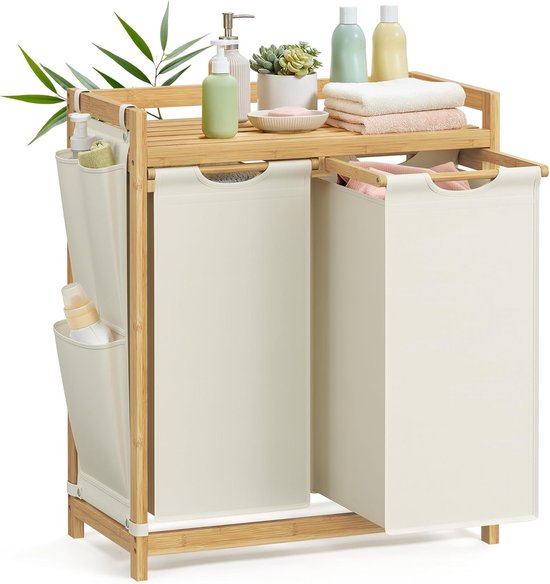 Bamboe wasmand met 2 off-white waszakken, een plank met badproducten, handdoeken en planten.