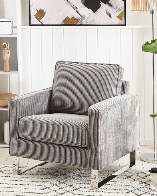 Grijze corduroy fauteuil met verchroomde metalen poten, in een woonkamer setting.
