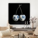 Delfts blauwe kersendecoratie aan de muur boven een wandmeubel met kandelaars.
