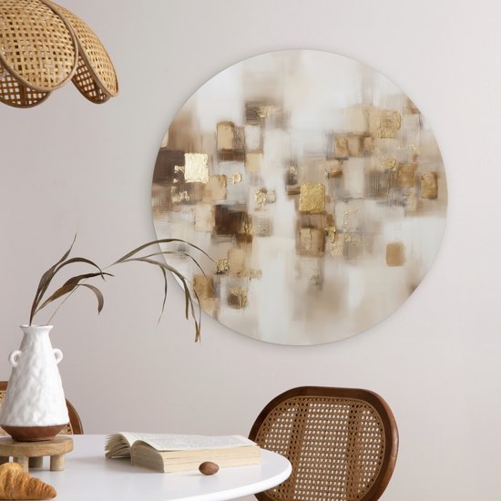 Abstracte muurcirkel met bruine en gouden vierkanten, hangend boven een witte tafel met een boek en een croissant.