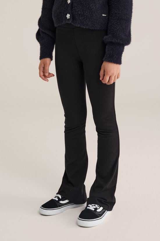 Model draagt een zwarte flared legging, gecombineerd met een donkerblauw pluizig vest en zwarte Vans sneakers.