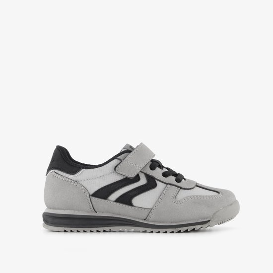 Grijze sneaker met zwarte zigzagstrepen, klittenbandsluiting en zwarte accenten.
