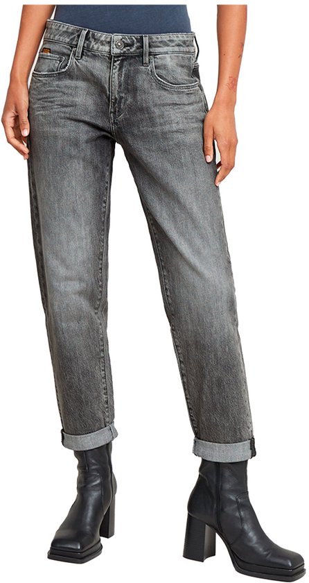 Model draagt een grijze jeans met opgerolde broekspijpen en zwarte laarzen.