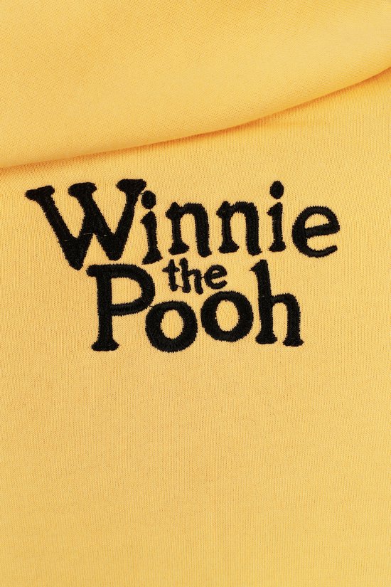Detail van geborduurde tekst 'Winnie the Pooh' in zwart op een gele hoodie.