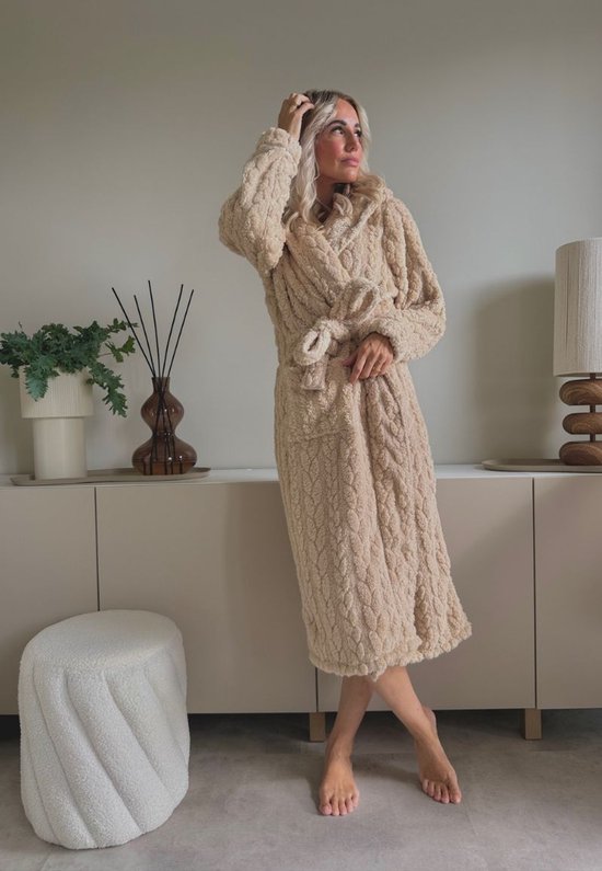 Lange beige badjas met capuchon van zacht fleece, model staat, handen bij haar.