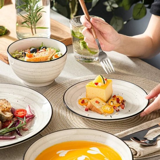 Wit servies met zwarte rand, met gebak, salade, soep en fruit. Textuur is zichtbaar op het servies.