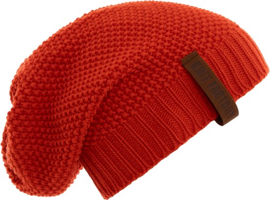 Een oranje gebreide muts met een bruin label van Knit Factory.