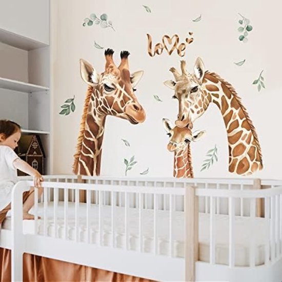 Stickers muraux représentant 3 têtes de girafe, des feuilles et le mot 'love' à côté d'un lit de bébé.