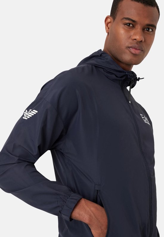 Close-up van de linker mouw van een marineblauw EA7 trainingsjack met gestreepte EA7 logo's.