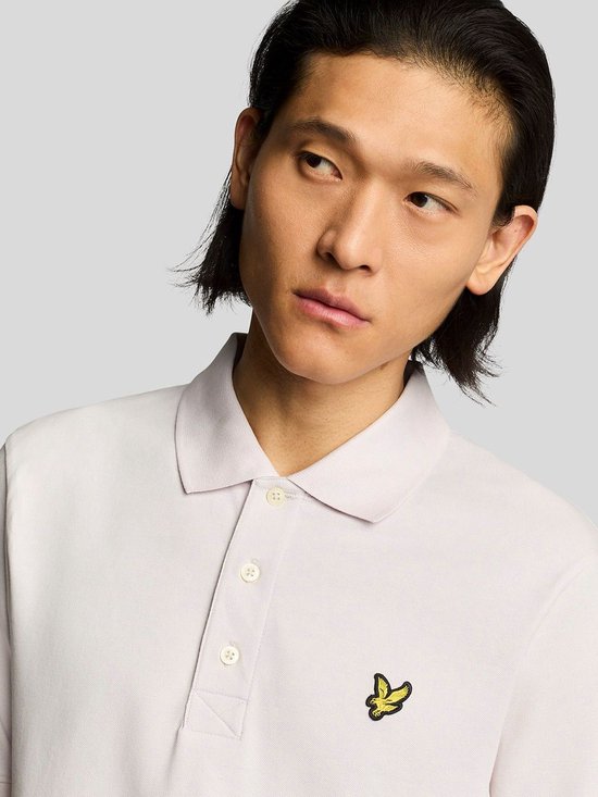 Close-up van lichtroze poloshirt met gele vogel-logo en witte knopen.