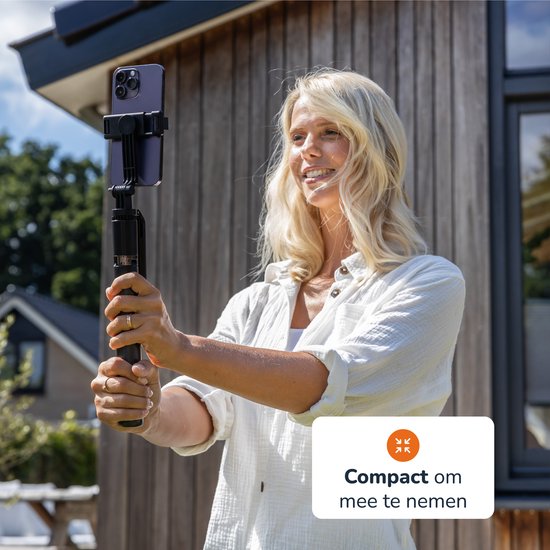 Vrouw met blond haar en witte blouse, staand buiten met een selfiestick. 'Compact om mee te nemen'.