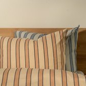 Twee gestreepte kussens op een bed met houten hoofdeinde. Een kussen met bruine strepen, een ander met blauwe strepen.