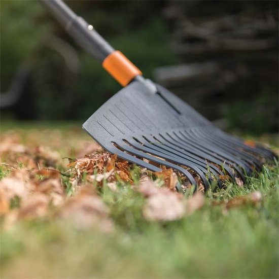 Zwarte Fiskars bladhark met oranje accent op gras met herfstbladeren.