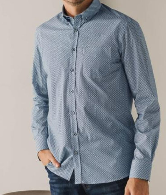 Man met lange blauwe overhemd met all-over print en borstzakje. Draagt jeans.