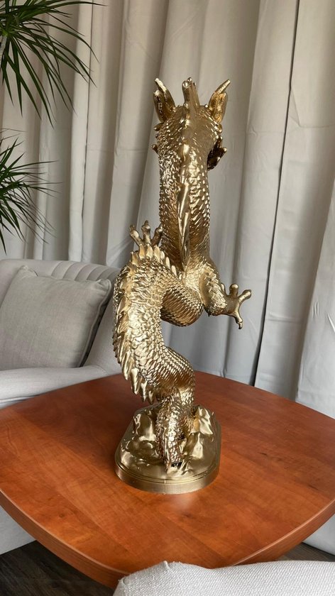 Gouden drakenbeeld, zittend op een houten tafel met planten op de achtergrond.