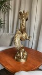 Gouden drakenbeeld, zittend op een houten tafel met planten op de achtergrond.