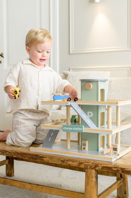 Jongetje met blond haar speelt met een pastelgroene houten speelgoedgarage op een houten bankje.