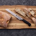 Een zilverkleurig broodmes met kartelrand en zwart handvat, liggend op een houten snijplank naast gesneden brood.