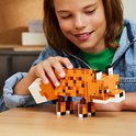 Un garçon à une table en bois joue avec un renard LEGO Minecraft constructible.