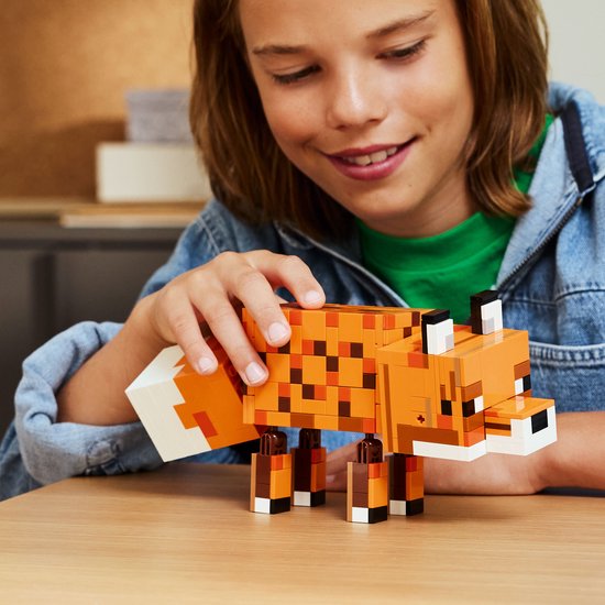 Un garçon à une table en bois joue avec un renard LEGO Minecraft constructible.