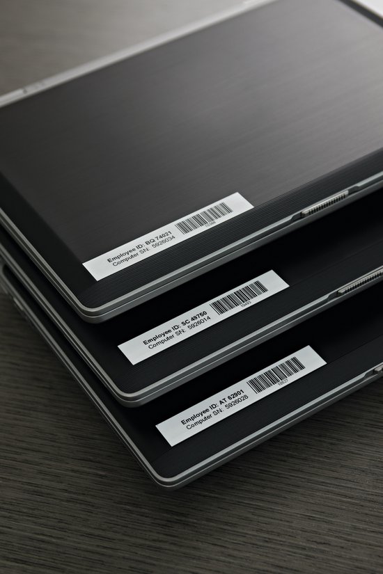 Stapel laptops met witte labels met serienummers en streepjescodes op de achterkant.