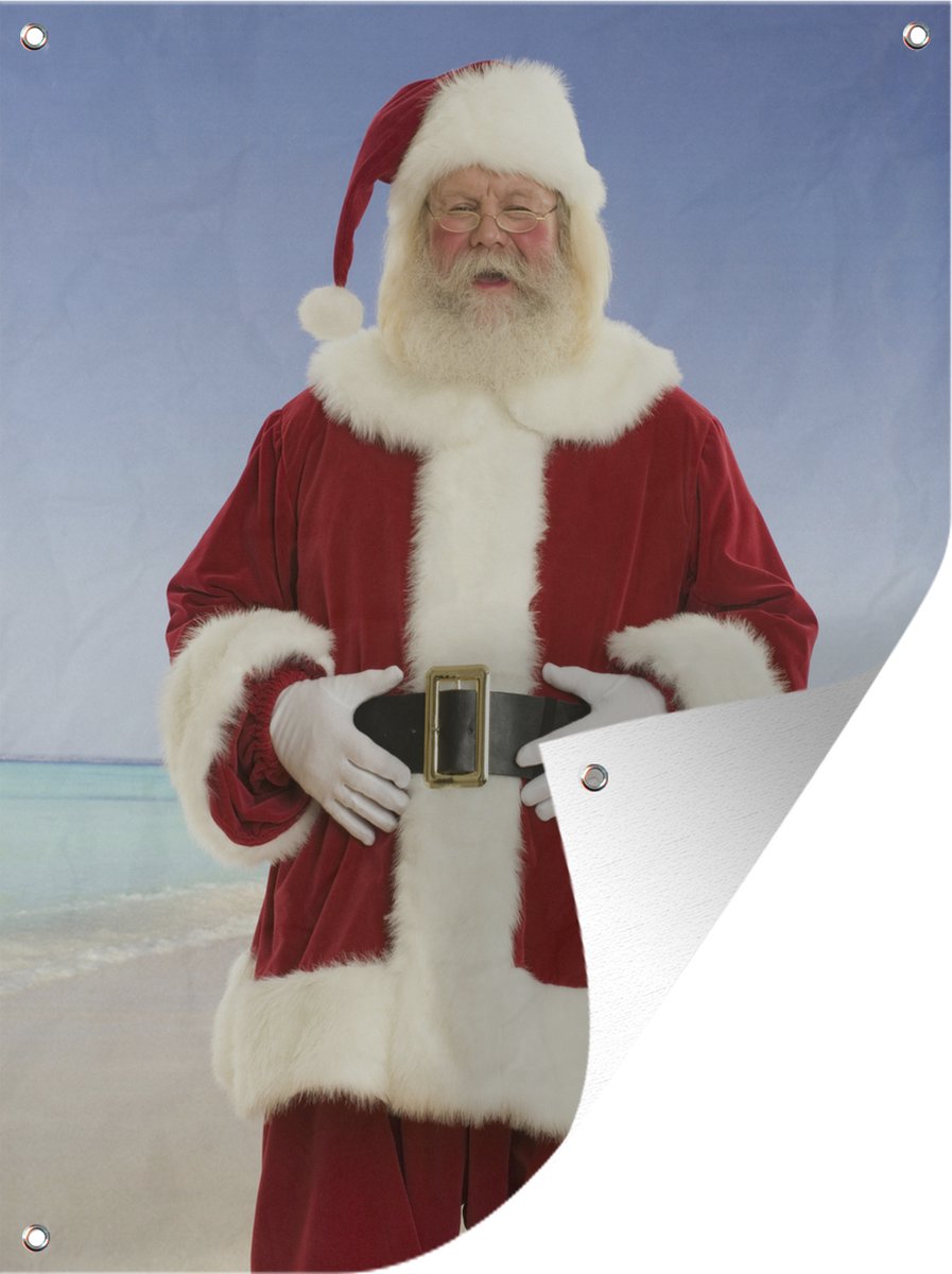 Tuinschilderij van de kerstman lachend op strand onder grijze hemel.