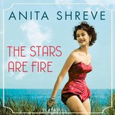 Boekomslag met de tekst 'THE STARS ARE FIRE ANITA SHREVE'. Een vrouw in rood badpak met gouden glans, lachend naar rechts, met de zee en gras op de achtergrond.