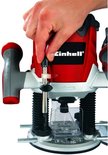 Hand stelt de Einhell bovenfrees in, met rode en zilveren behuizing.