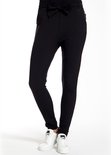 Een vrouw in een zwarte broek met hoge taille, strikceintuur en witte sneakers.