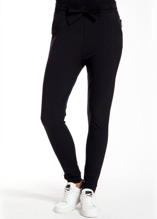 Een vrouw in een zwarte broek met hoge taille, strikceintuur en witte sneakers.