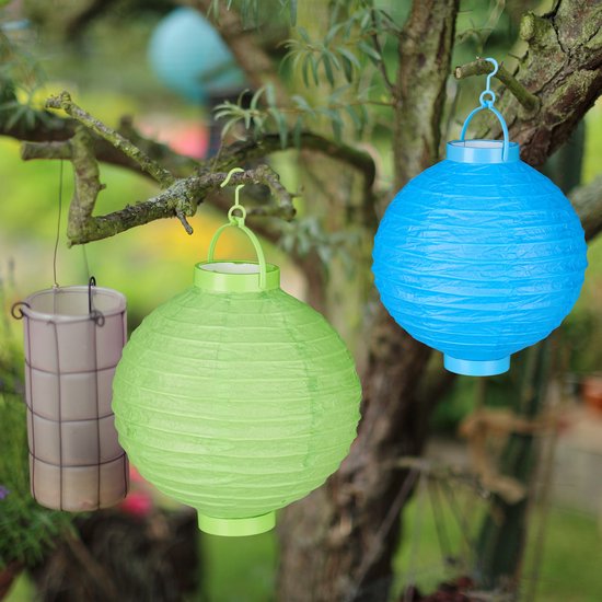 Twee groene en blauwe papieren lampionnen hangen aan een boom in een tuin.