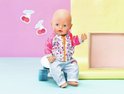 BABY born pop in roze jasje met print en lichtblauwe broek met regenboog. Zittend op een skateboard.