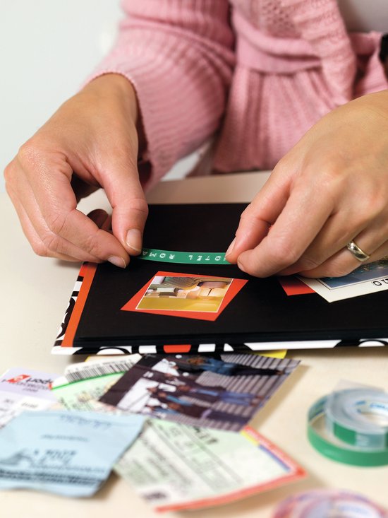 Vrouw plakt een zelfgeplakte letter "HOTEL" op een zwart album met foto's en tickets.