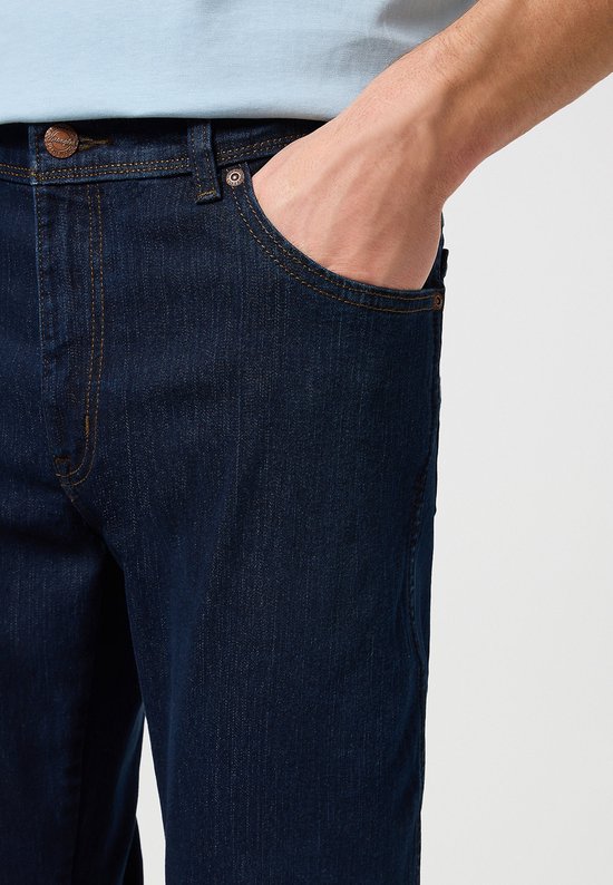 Man met een lichte blauwe blouse, in een donkerblauwe Wrangler jeans.